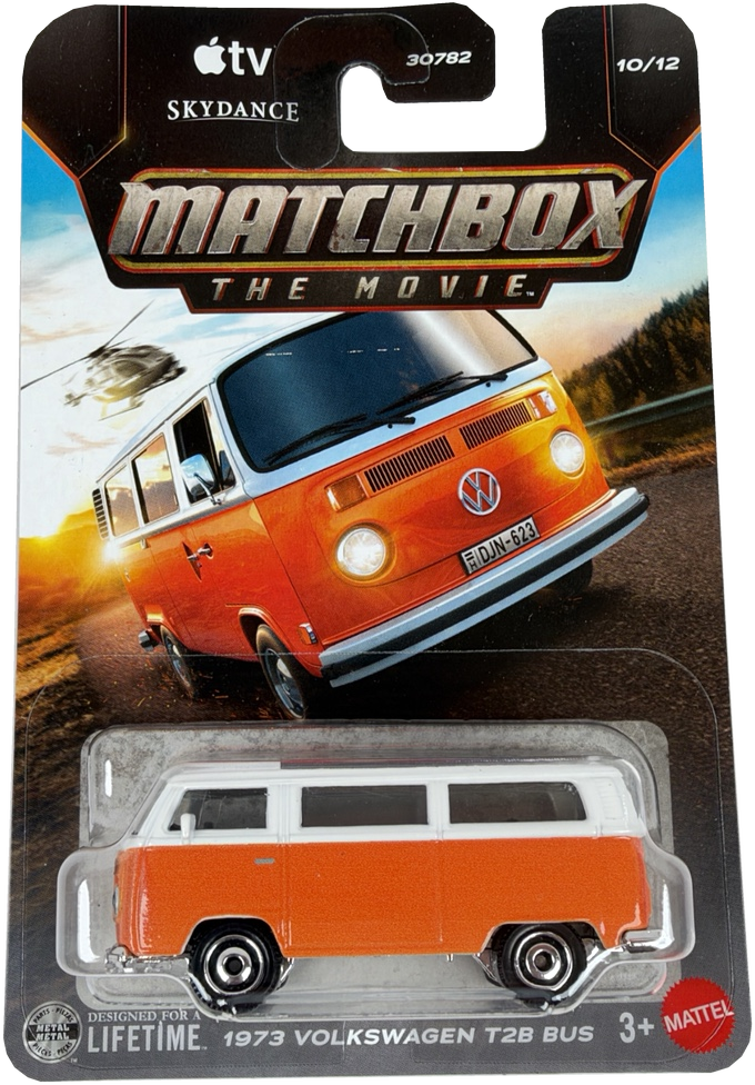 Matchbox The Movie diecast toy car of a 1973 Volkswagen T28 Bus, packaged on its original card. The bus is orange with a white roof, and the packaging card features artwork of the iconic orange and blue bus in a scenic setting.  Card has a small factory print error.