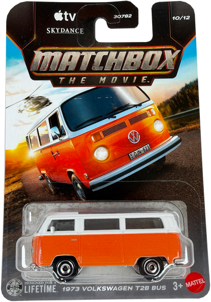 Matchbox The Movie diecast toy car of a 1973 Volkswagen T28 Bus, packaged on its original card. The bus is orange with a white roof, and the packaging card features artwork of the iconic orange and blue bus in a scenic setting.  Card has a small factory print error.